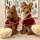 Two plush fox toys wearing red outfits with white lace details against a decorative wall.