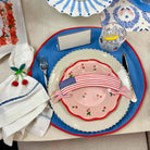 Table setting with decorative plates, napkin, and cutlery on a white tablecloth.