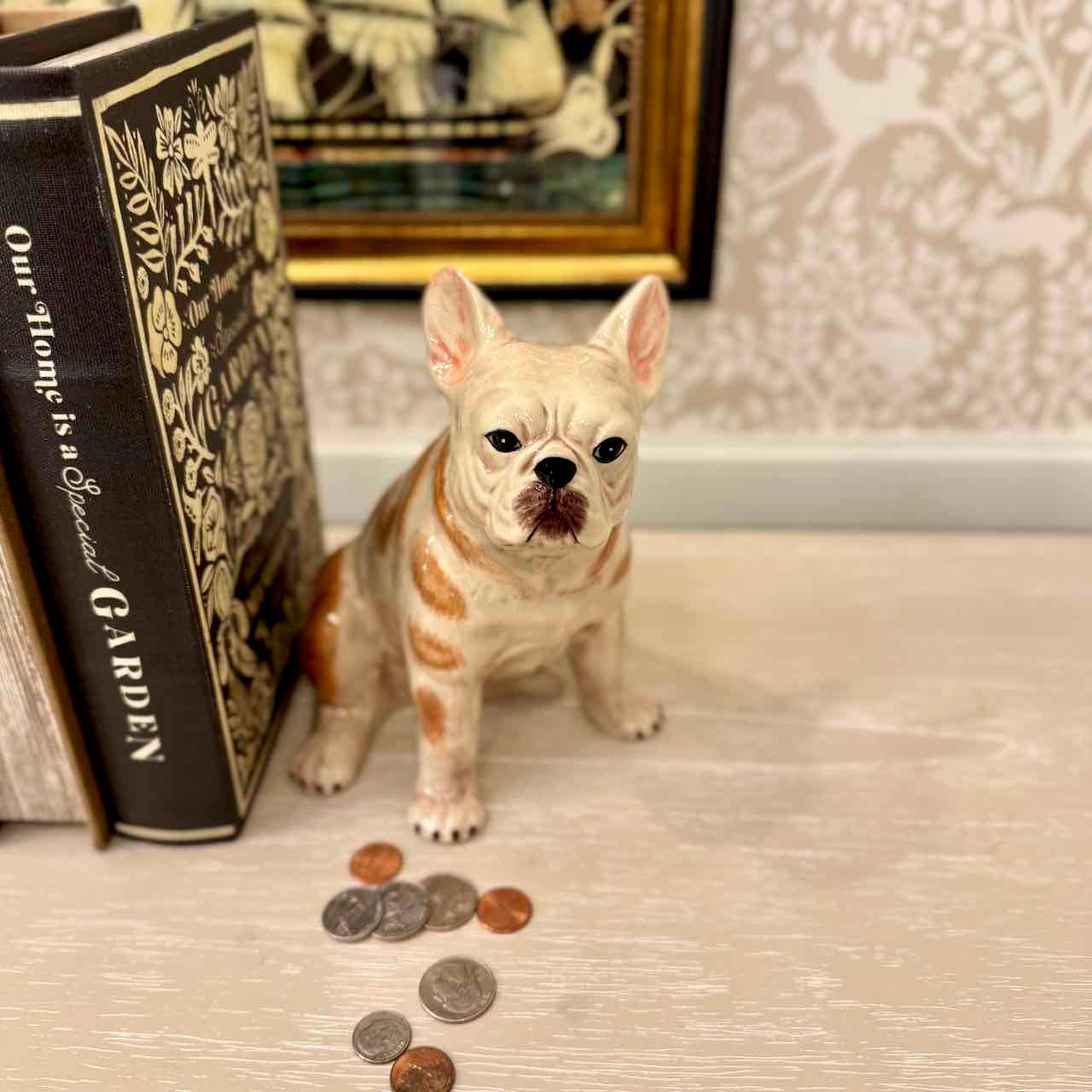 Small dog figurine with coins on a surface, next to a book titled 'Our home is a Special Garden'.