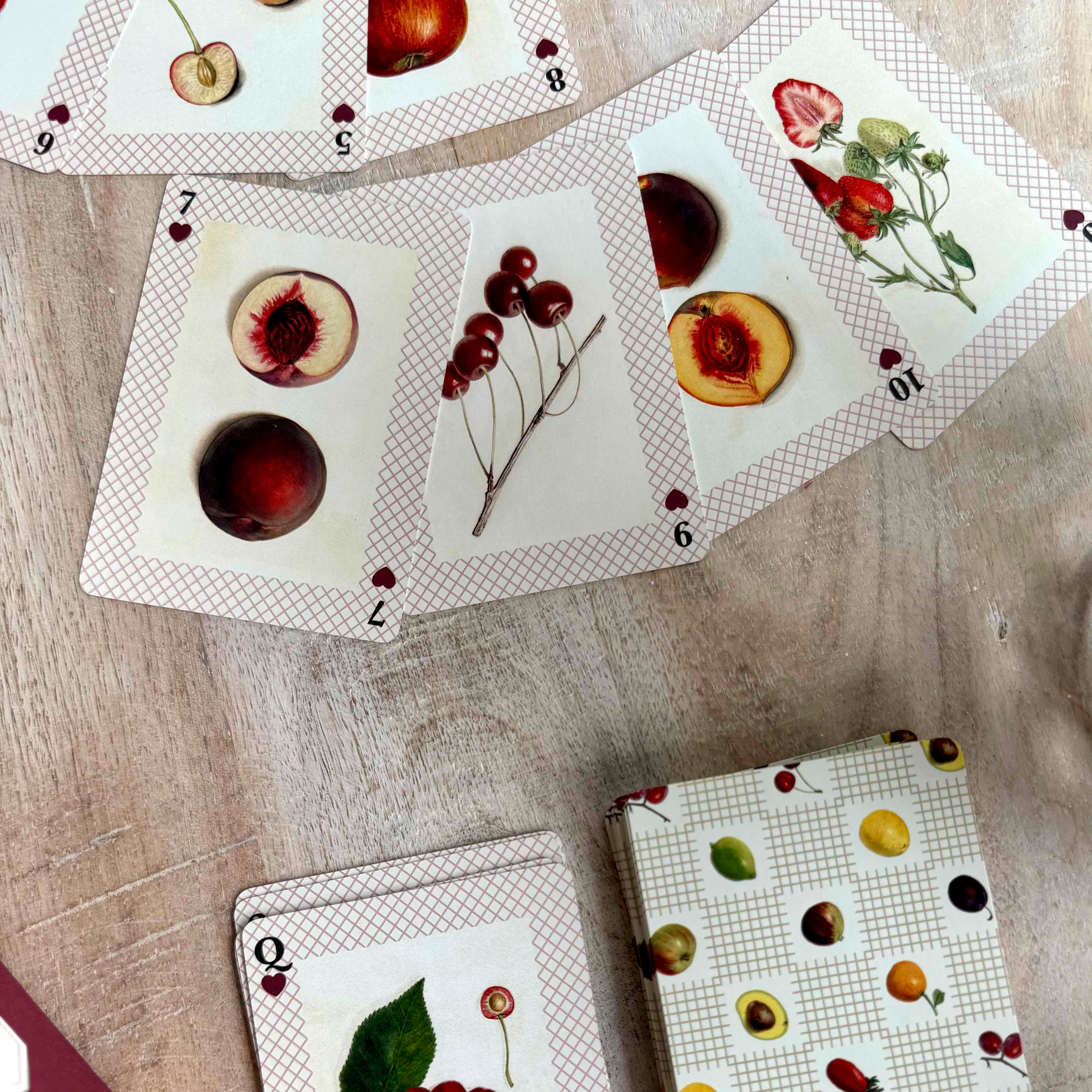 Playing cards with fruit and floral designs on a wooden surface