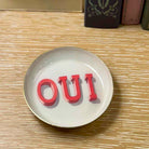 Round white plate with red 'OUI' text on a wooden surface
