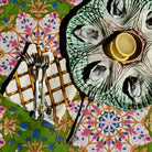 An overhead styled shot of oysters served on a green scalloped ceramic platter with lemon slices, alongside silver forks on a patterned tablecloth.