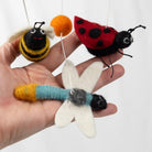 Hand holding three felt insect toys against a white background
