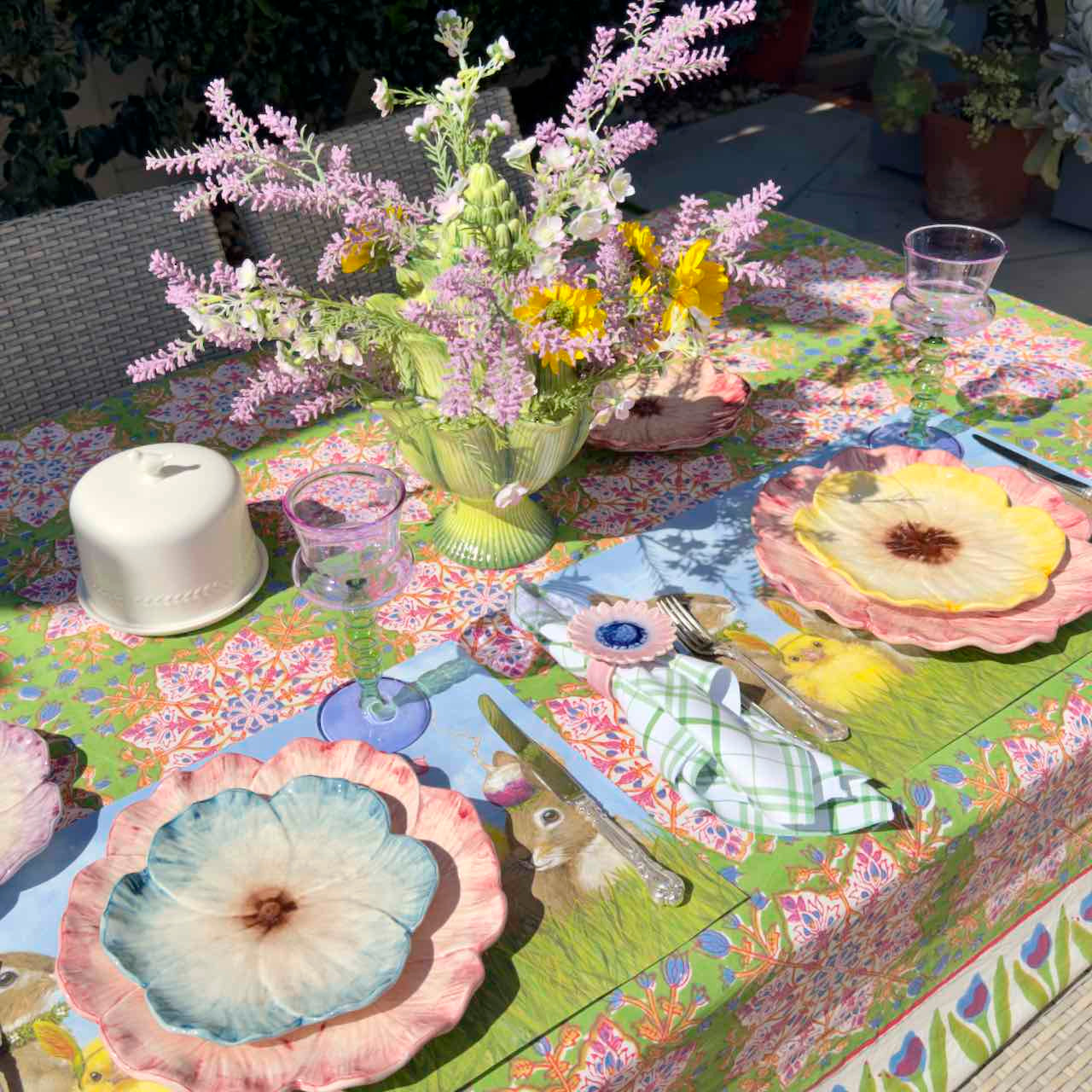 Decorative table setting with floral tablecloth, plates, and flowers.