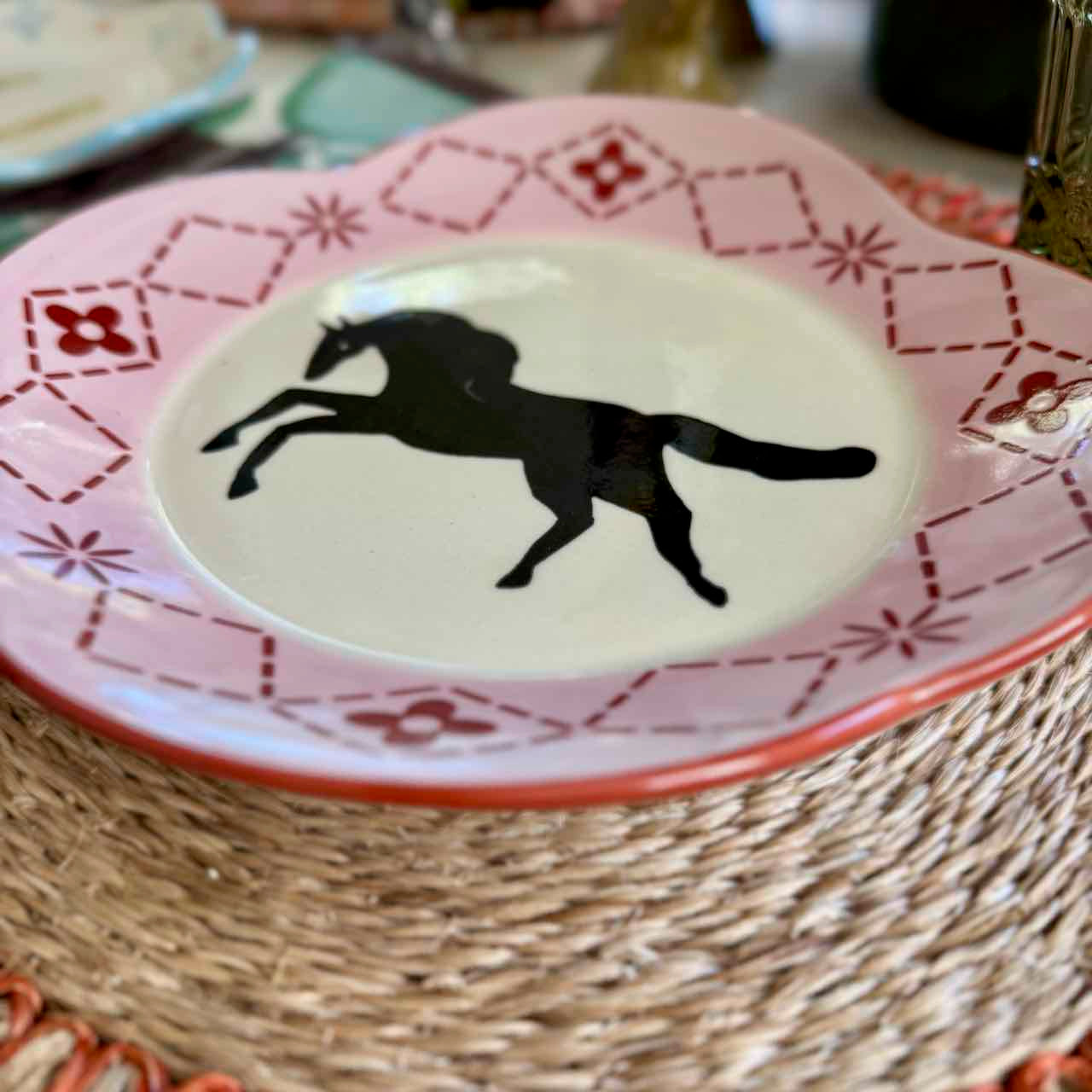 Decorative plate with a black horse silhouette on a pink and red patterned rim