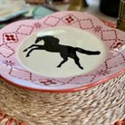 Decorative plate with a black horse silhouette on a pink and red patterned rim