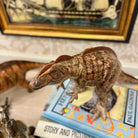 Model of a dinosaur on top of a book with a framed picture in the background