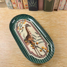 Decorative oval plate with a giraffe design on a wooden surface with books in the background