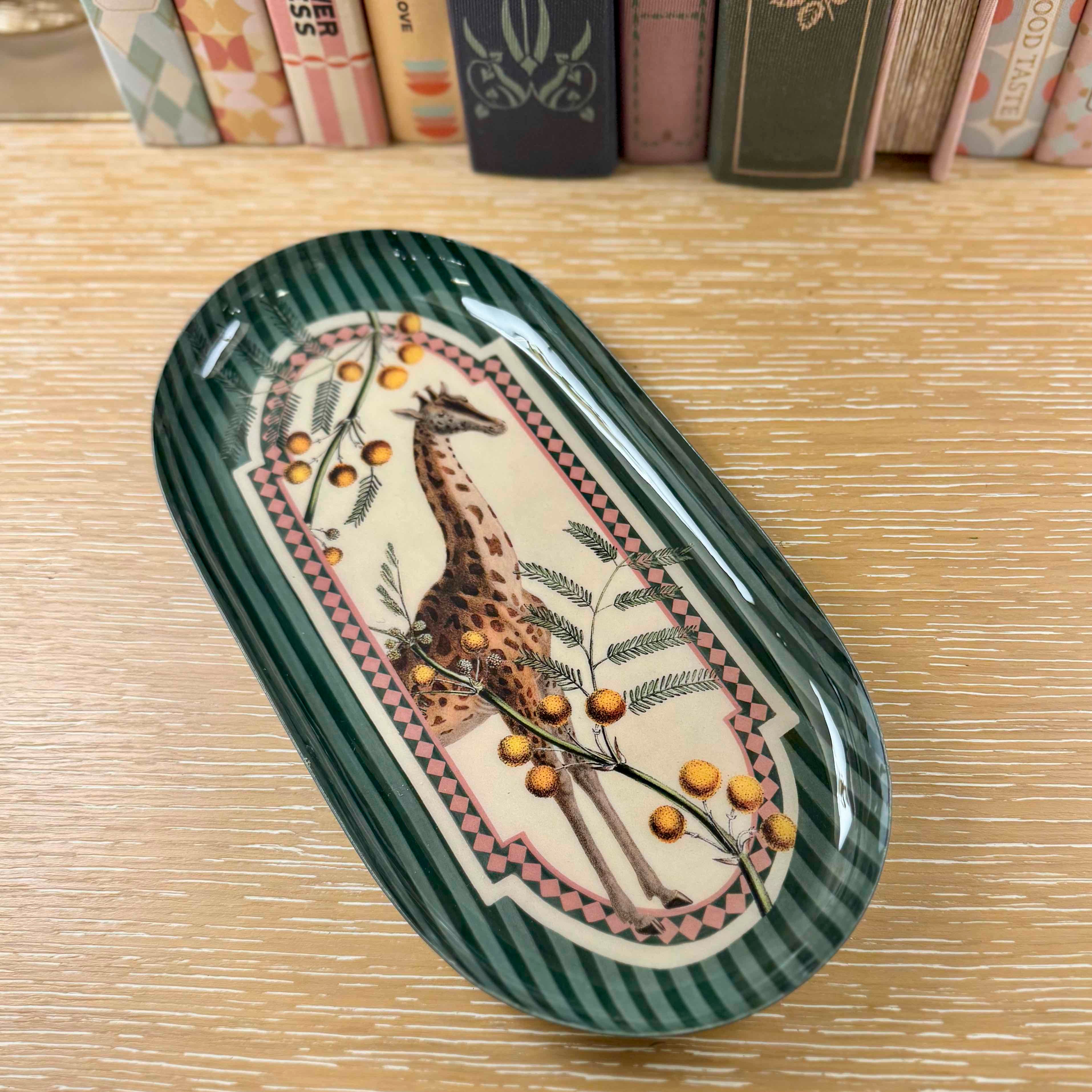Decorative oval plate with a giraffe design on a wooden surface with books in the background