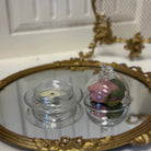 Decorative glass container with pink flower inside on a mirror surface.