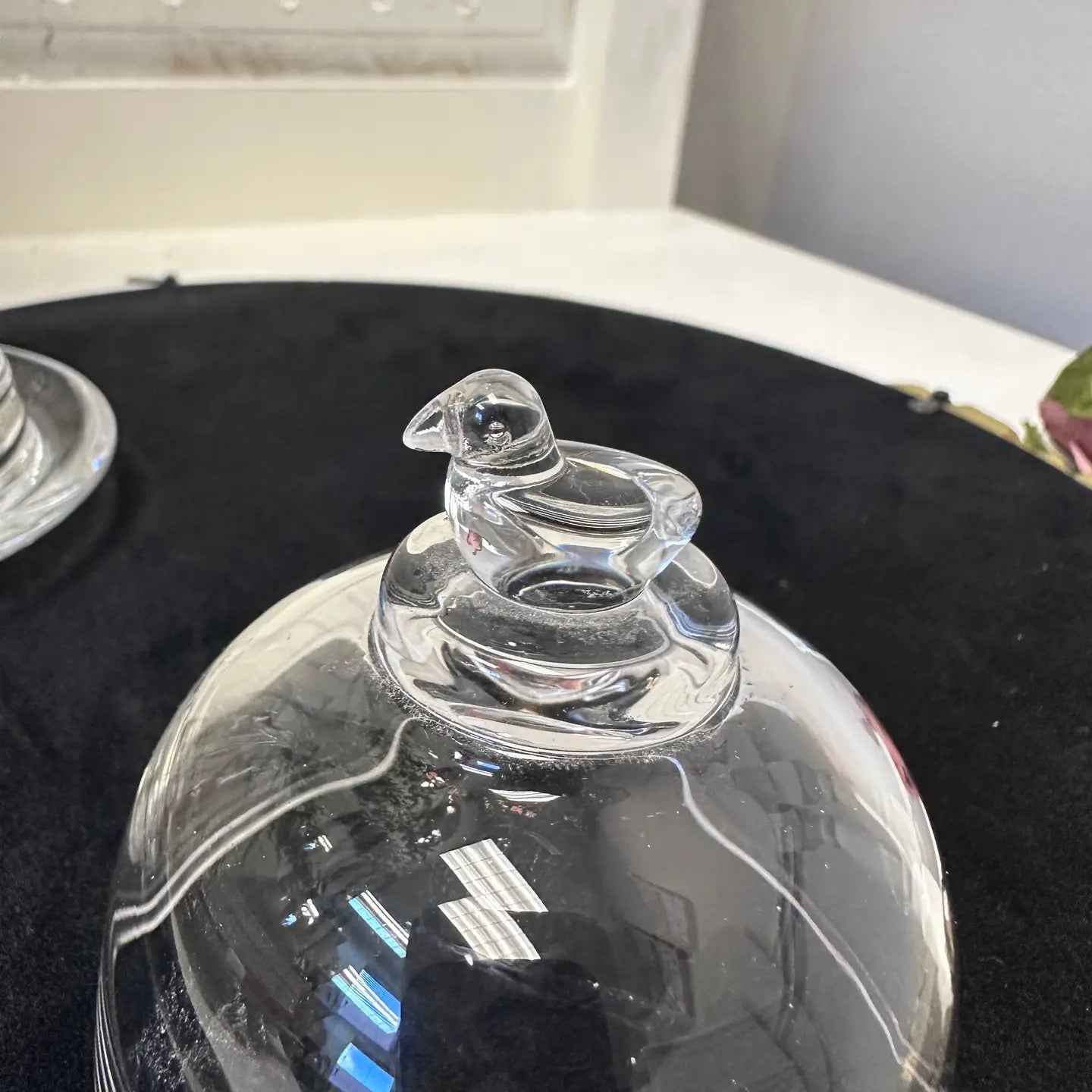 Clear glass dome with a bird-shaped finial on a black surface