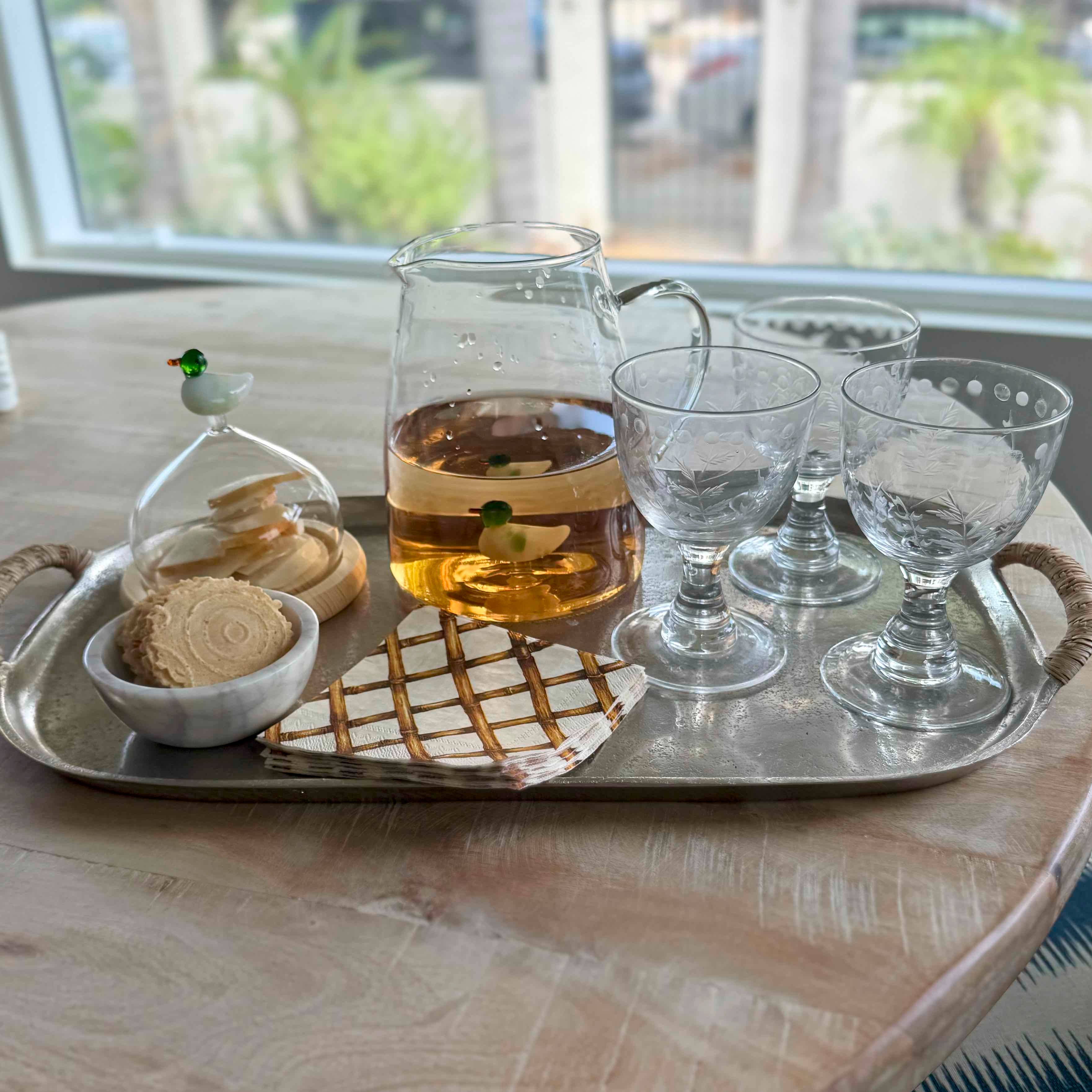 Tray with a carafe, glasses, and cookies on a table with a window view.