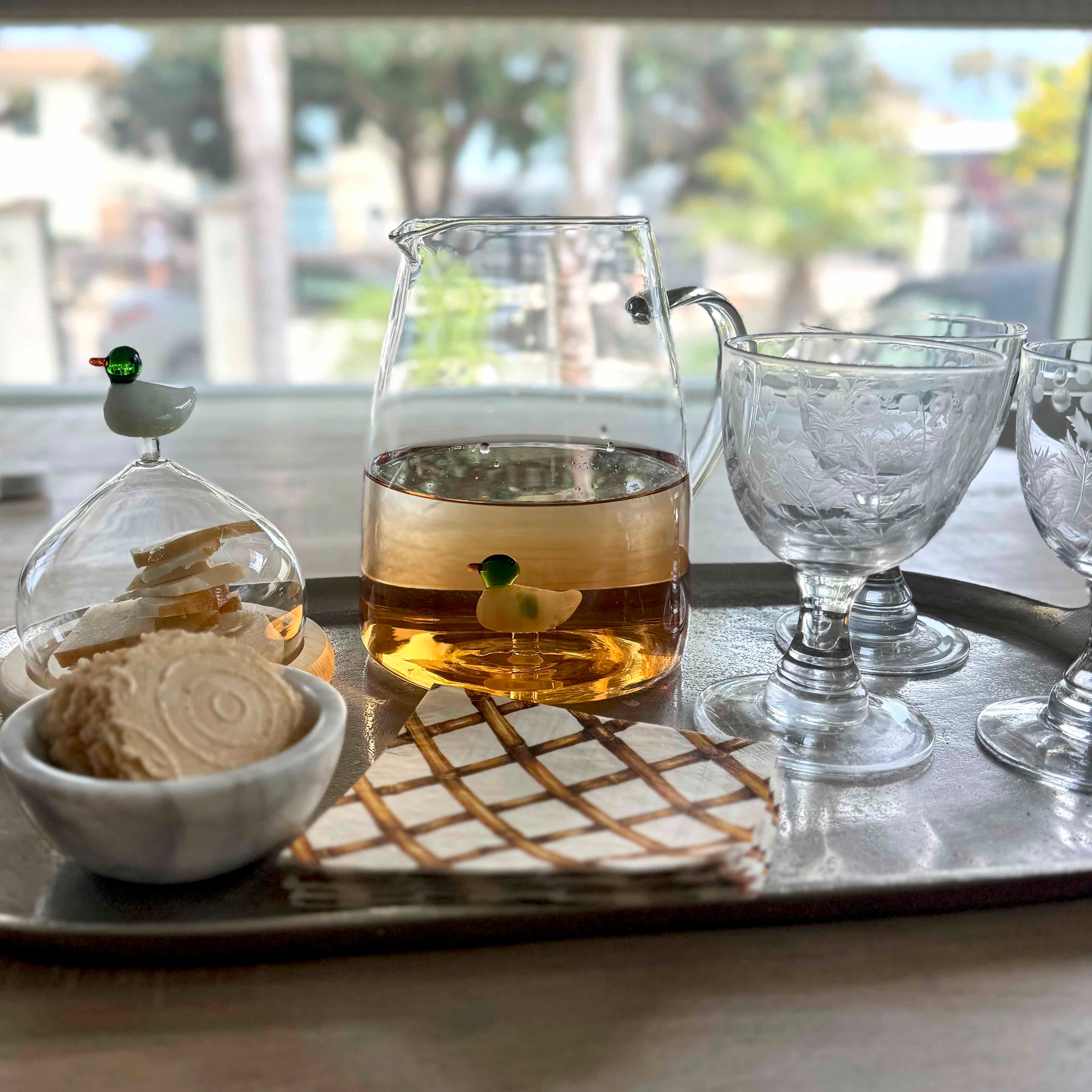 Tea set with teapot, glasses, and cookies on a tray by a window