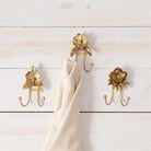 Three gold floral-patterned hooks on a wooden wall with a beige towel draped over one of them.