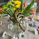 Decorative vase with a gold leaf design on a table with flowers and daisies.