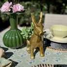Gold rabbit-shaped vase on a table with a green vase and flowers in the background