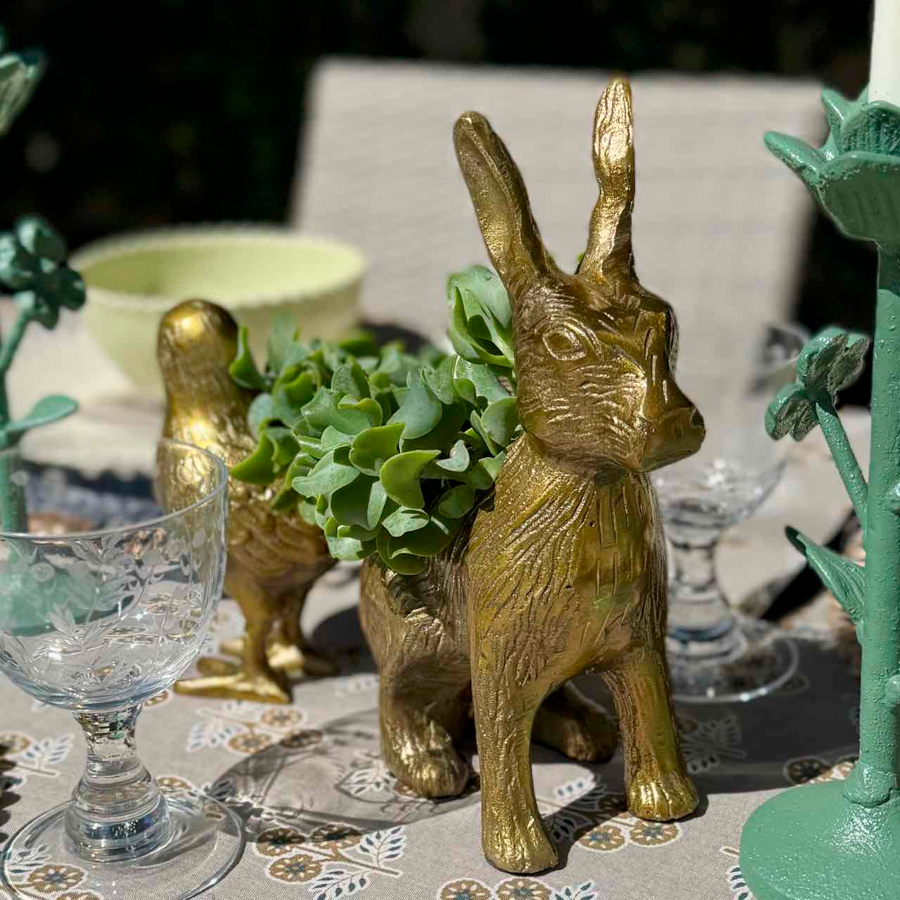 Gold rabbit-shaped planters on a table with decorative glasses and greenery.