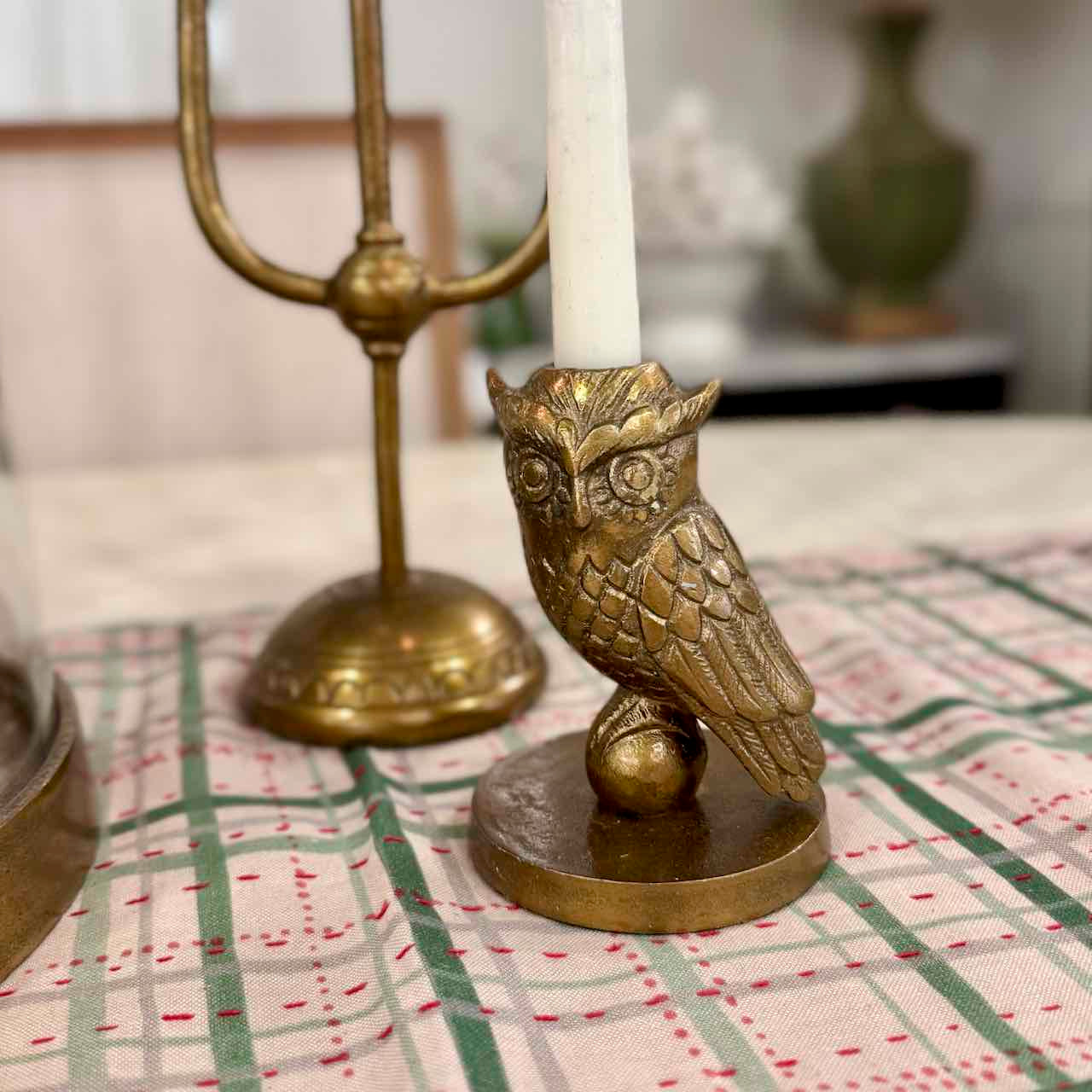 Bronze owl candle holder with a white candle on a checkered tablecloth.