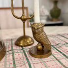 Bronze owl candle holder with a white candle on a checkered tablecloth.