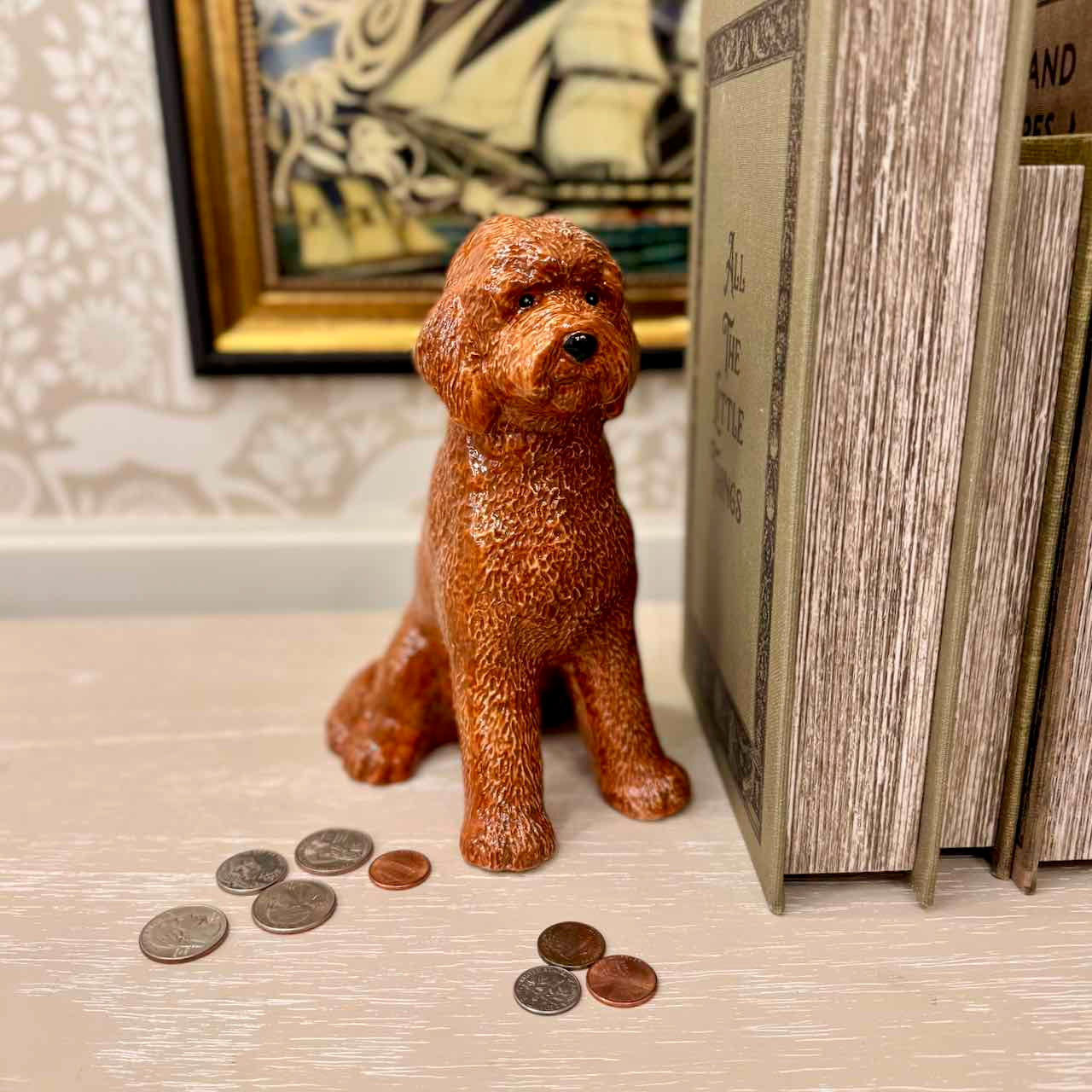 Brown dog-shaped piggy bank with coins on a surface, with a book and decorative item in the background.