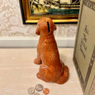 Dog-shaped money box with coins on a surface, framed artwork in the background