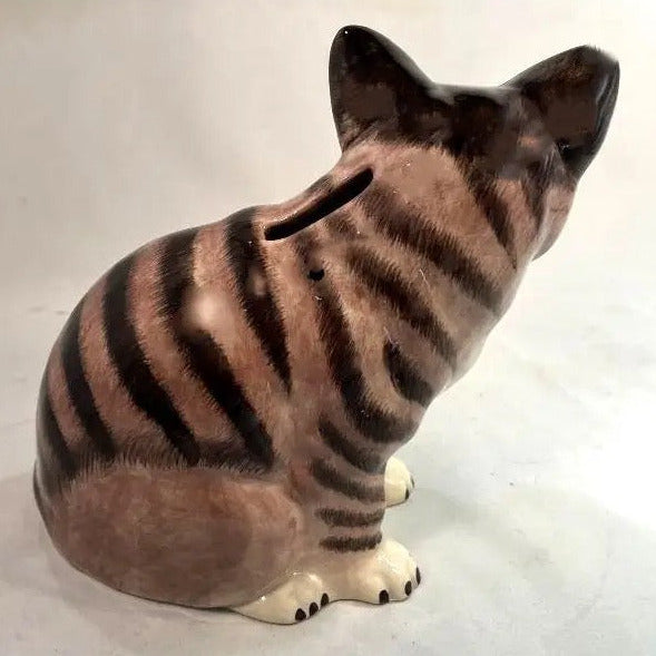 A ceramic cat-shaped pig bank with brown and beige tabby stripes, shown from a rear three-quarter view on a light gray background.