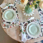 Table setting with floral tablecloth, plates, and cutlery on a wooden table.