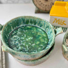 Green ceramic bowl with soup on a white surface, next to a carton of milk.