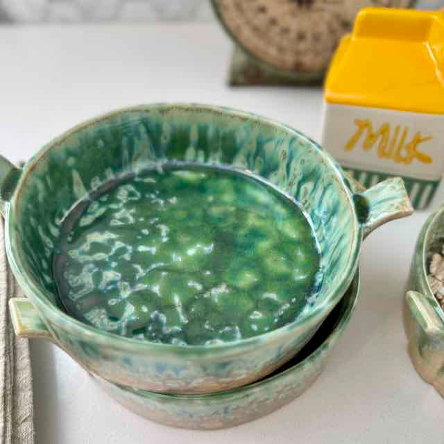 Green ceramic bowl with soup on a white surface, next to a carton of milk.