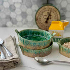 Green ceramic bowls on a kitchen counter with utensils and a clock in the background.