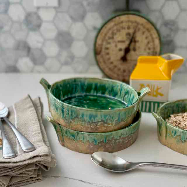 Green ceramic bowls on a kitchen counter with utensils and a clock in the background.