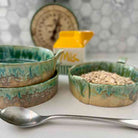 Set of ceramic bowls with green glaze on a white surface, with a carton of milk in the background.