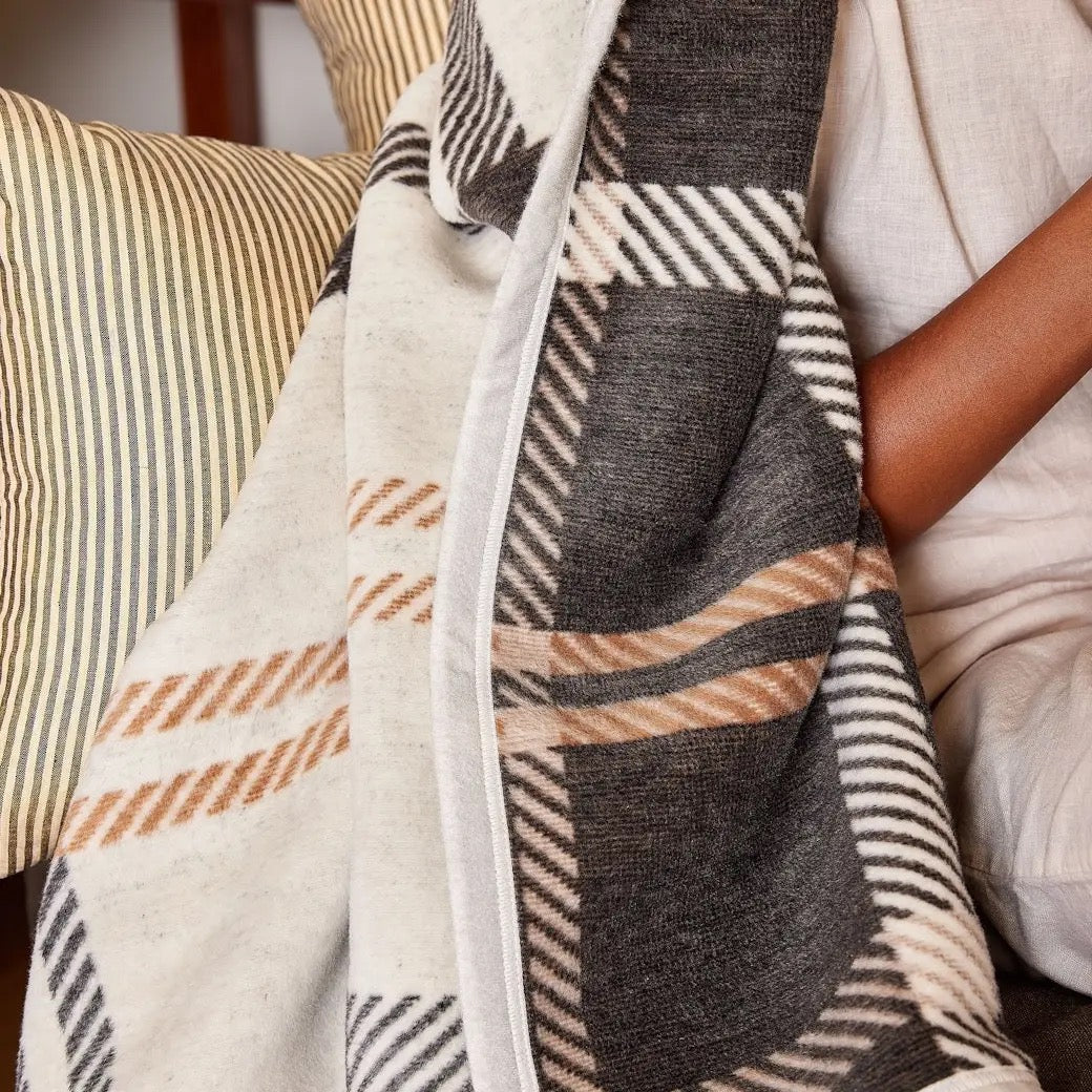 Person wrapped in a plaid blanket with a striped pillow in the background