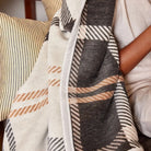 Person wrapped in a plaid blanket with a striped pillow in the background