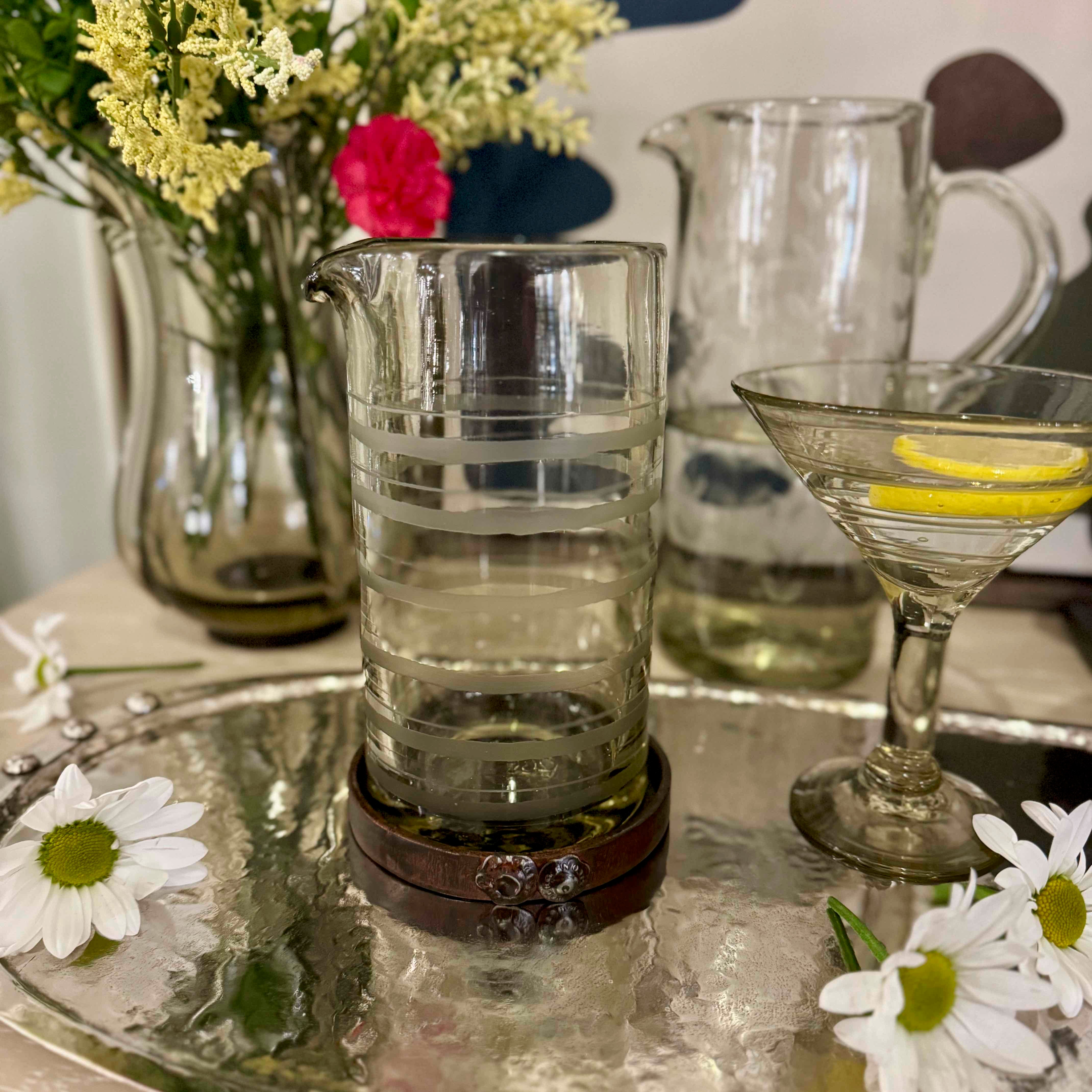 Clear glass measuring cup on a coaster with flowers and a pitcher in the background.