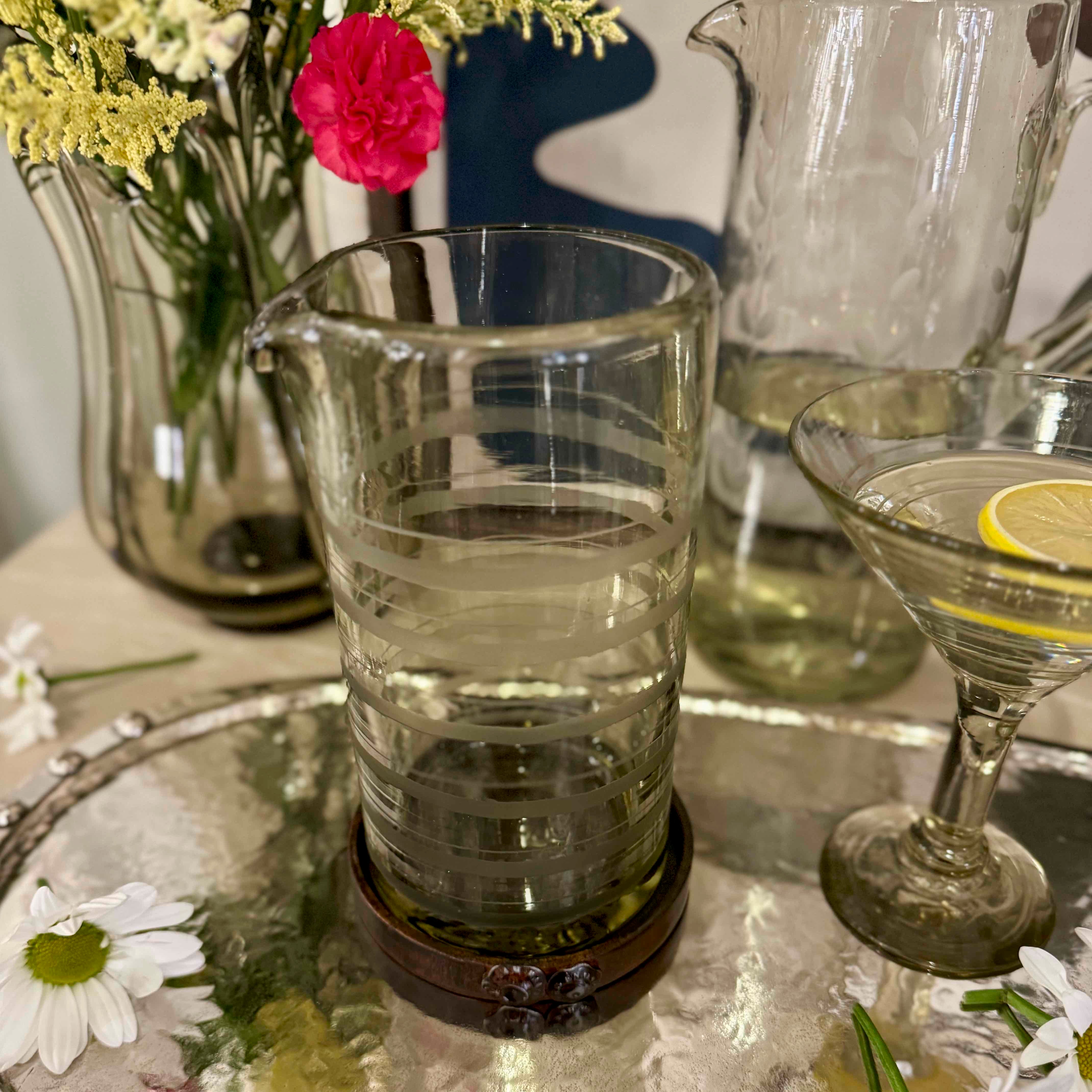Clear glass with water on a reflective surface, surrounded by flowers and another glass.
