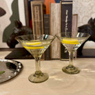 Two martini glasses with lemon slices on a table with books in the background