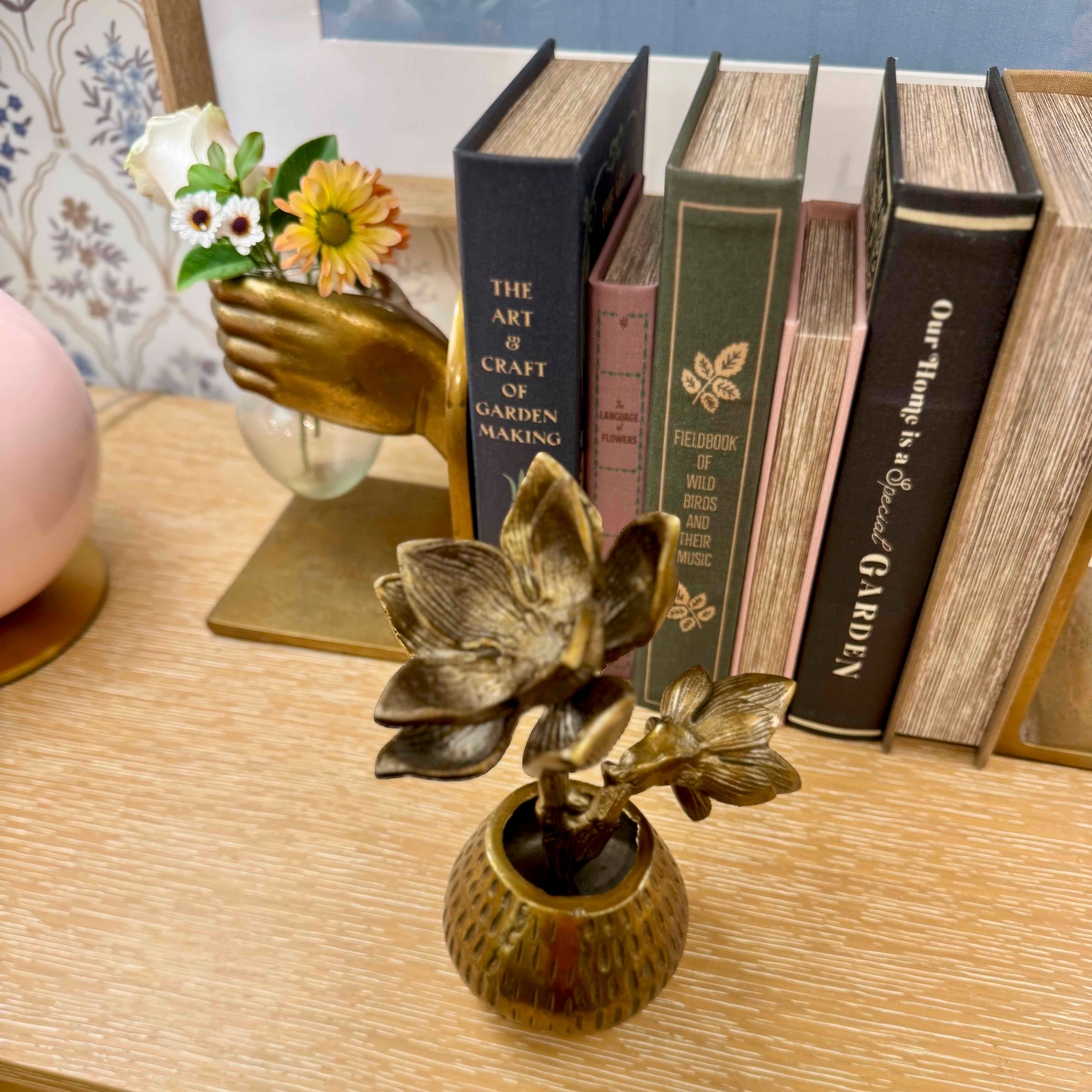 Bronze flower sculpture on a table with books and a small plant.