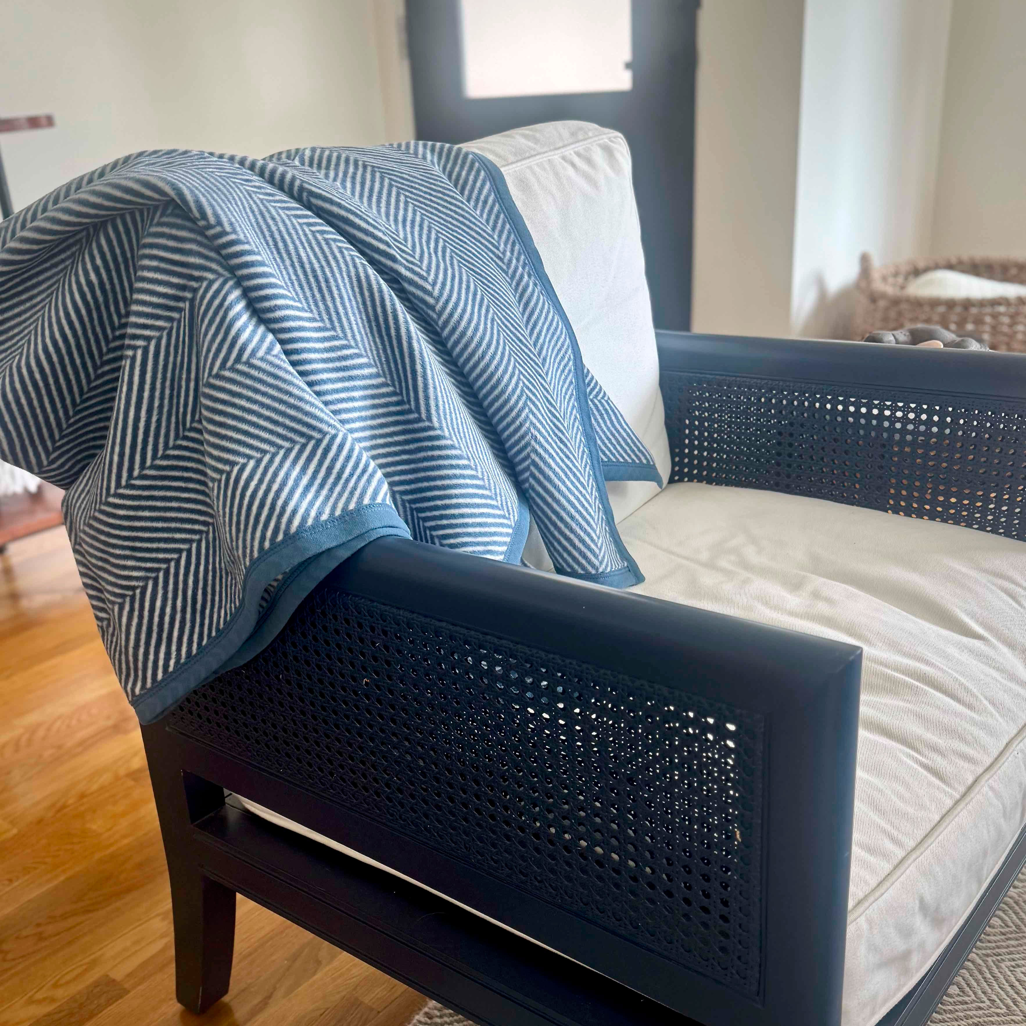 Blue and white patterned blanket draped over a blue wicker chair with a neutral background.