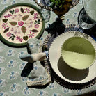Decorative table setting with floral plate, green bowl, and patterned napkin on a floral tablecloth.