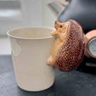 Ceramic mug with a hedgehog-shaped handle on a table.