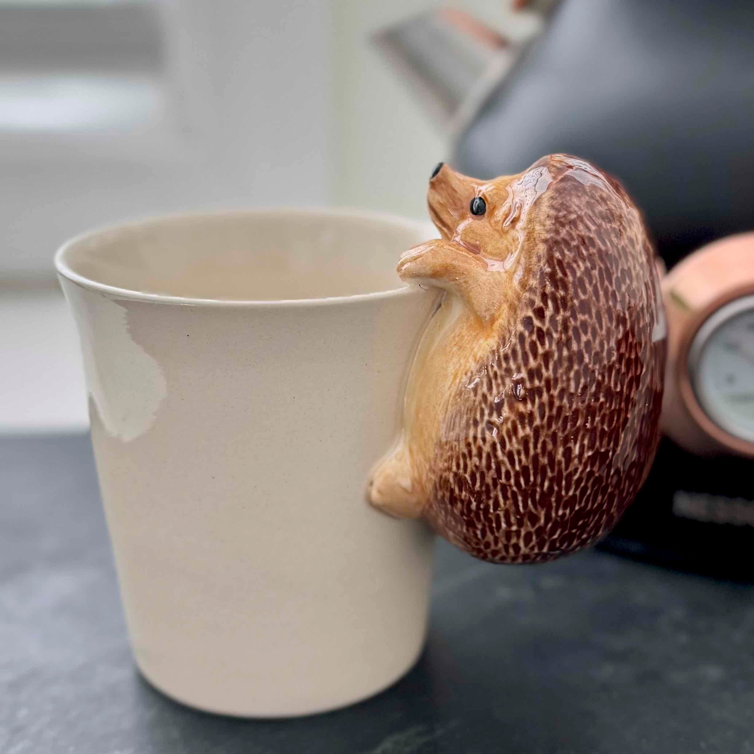 Ceramic mug with a hedgehog-shaped handle on a table.