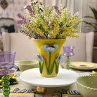 Decorative table setting with a yellow vase holding flowers on a white plate.
