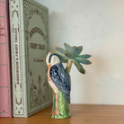 Ceramic bird figurine with a succulent on a wooden surface next to books.