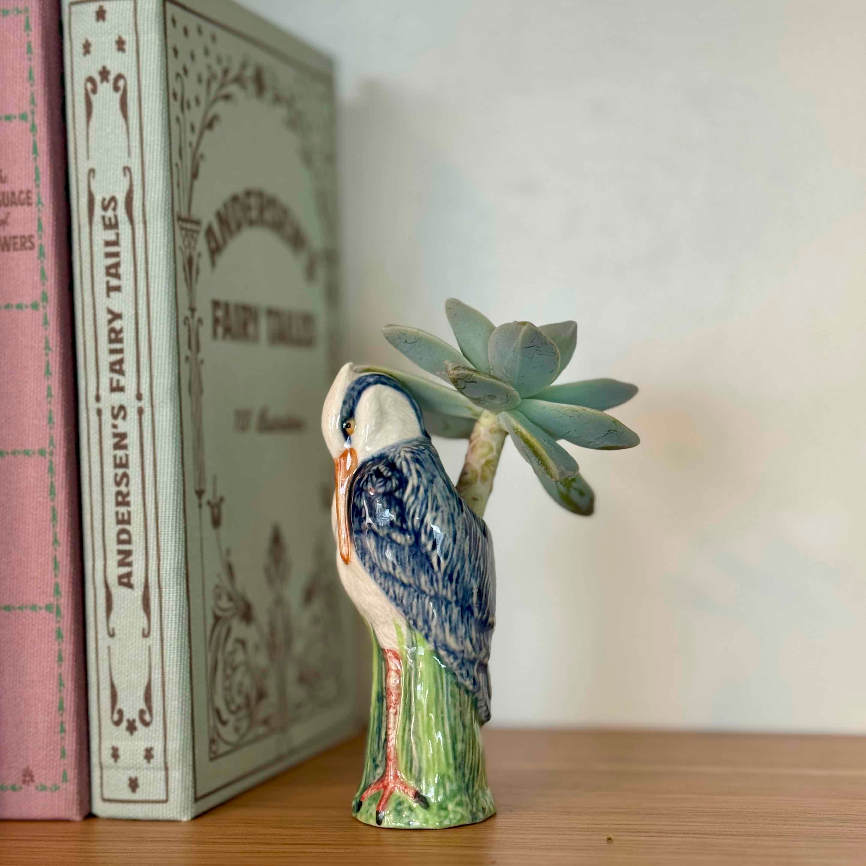 Ceramic bird figurine with a succulent on a wooden surface next to books.