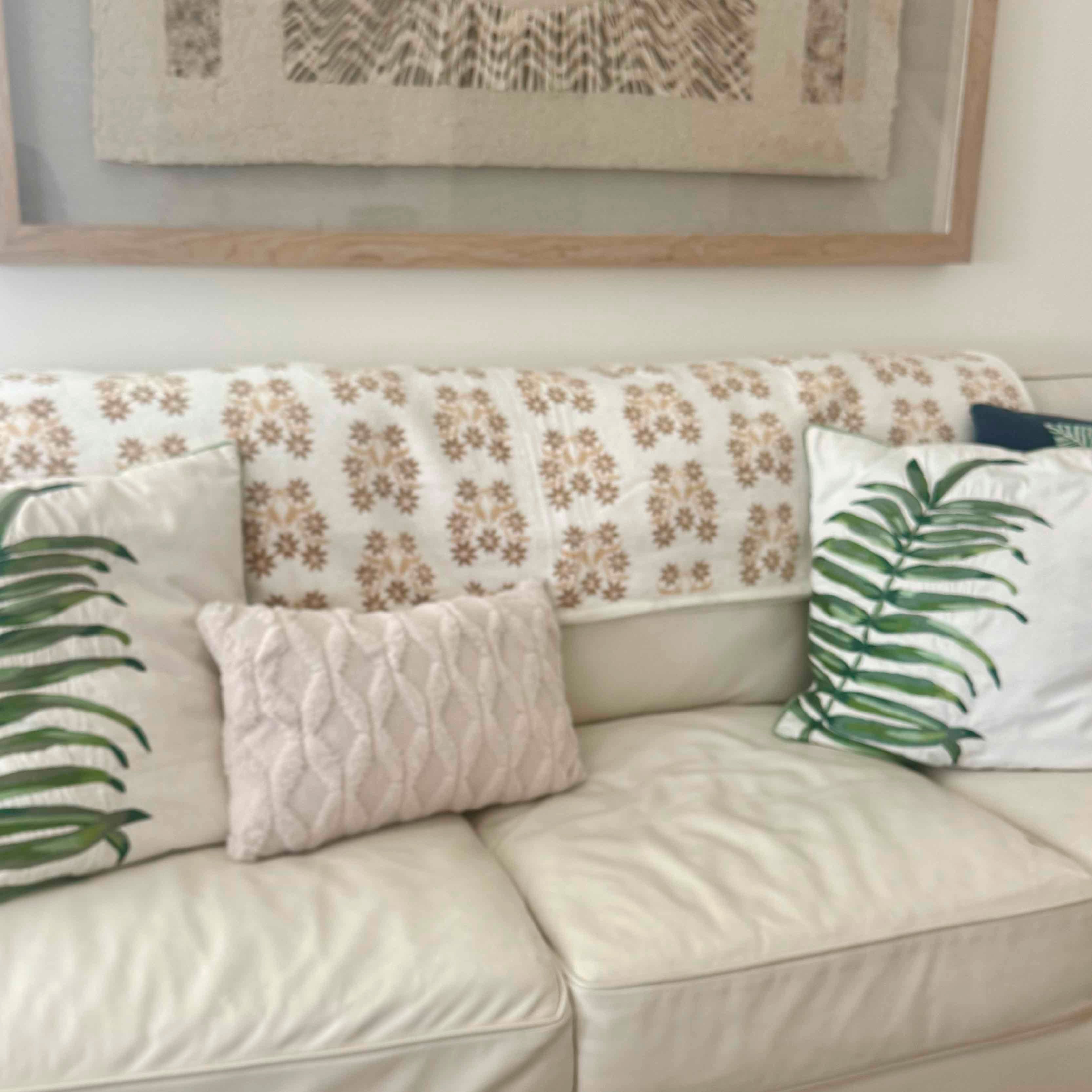Beige sofa with floral and leaf-patterned cushions, framed artwork in the background.