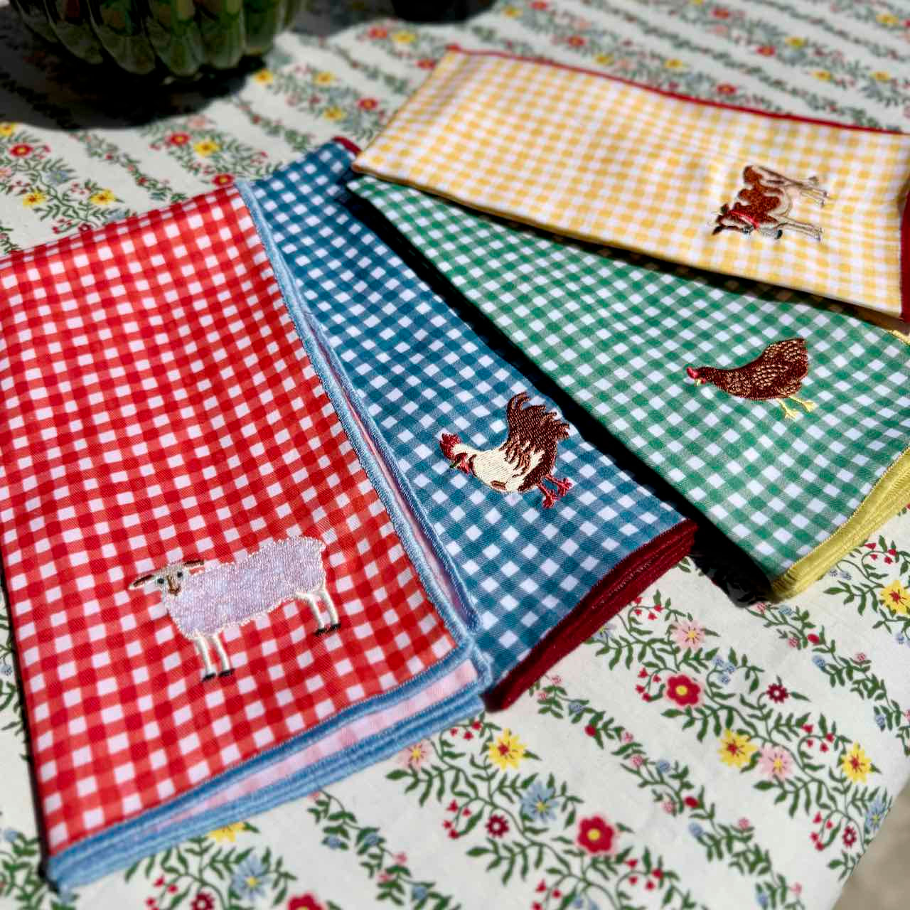Collection of checkered and floral patterned towels with embroidered animals on a table.