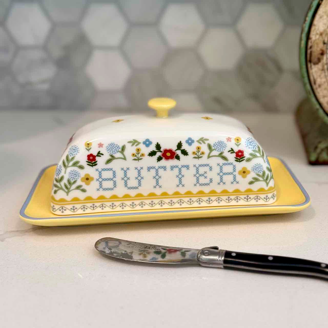 Decorative butter dish with floral patterns and a knife on a kitchen counter.