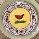 Decorative plate with a rooster design on a yellow background, surrounded by floral patterns.