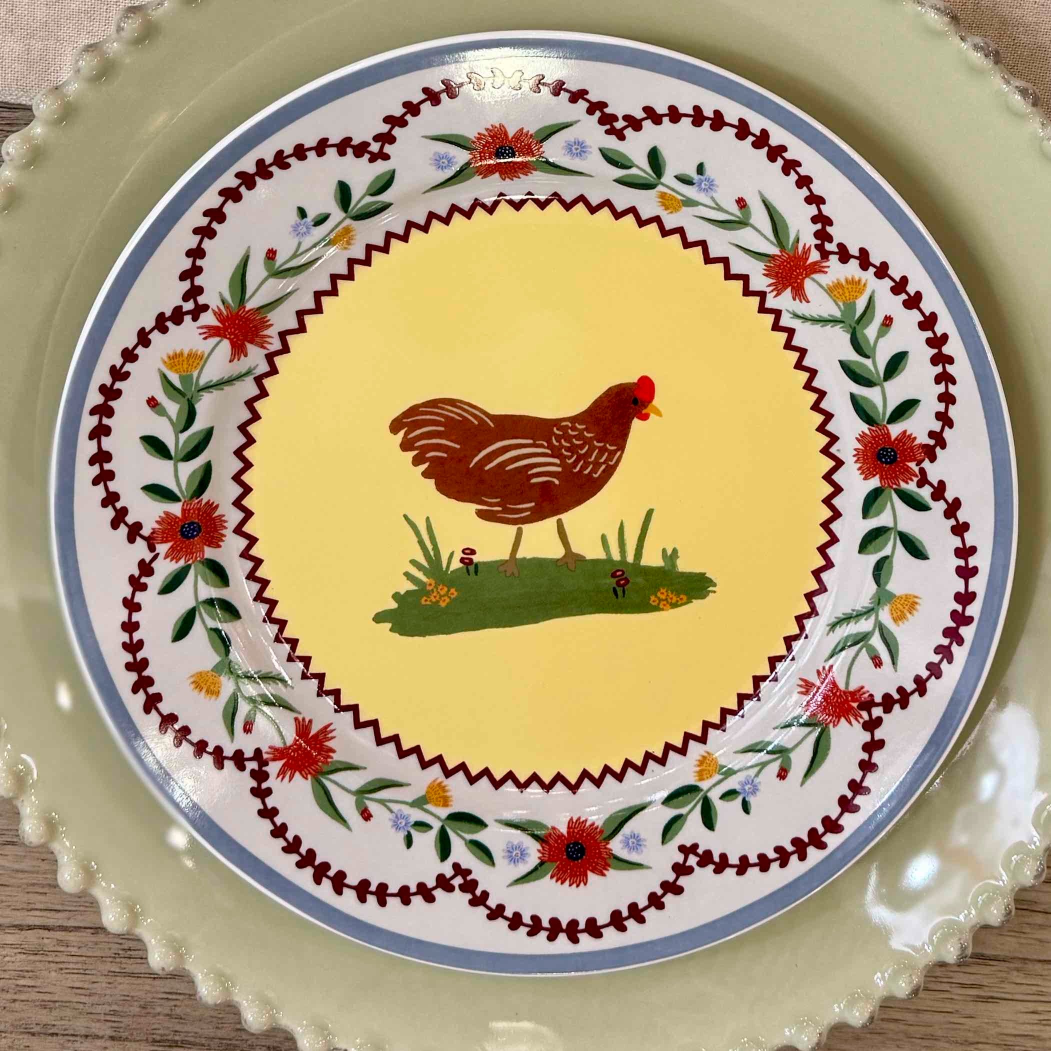 Decorative plate with a rooster design on a yellow background, surrounded by floral patterns.